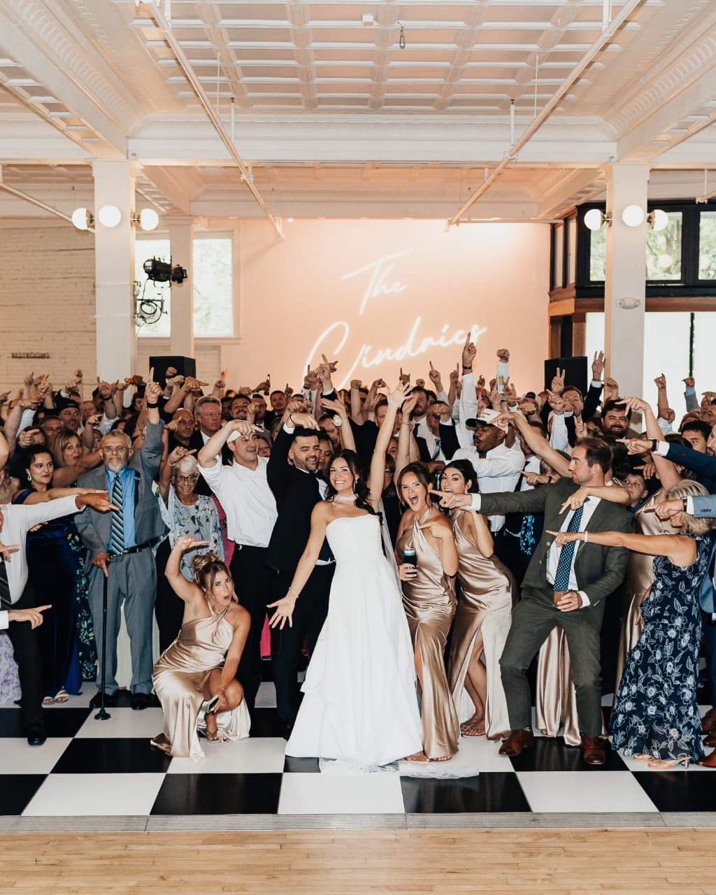 Bride and groom at the center of their full wedding dance floor, surrounded by cheering guests